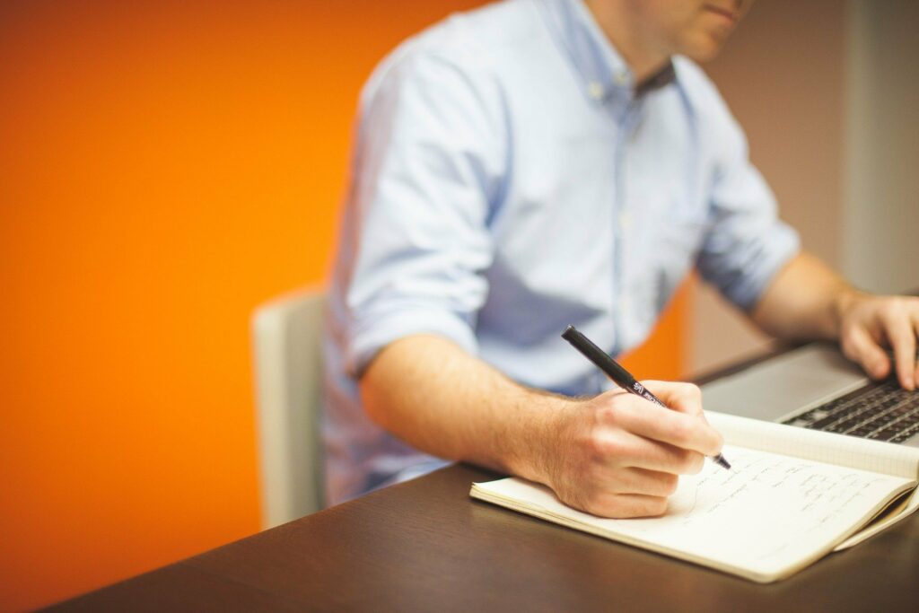 imagen de profesional scrum master escribiendo en una libreta y en un portatil